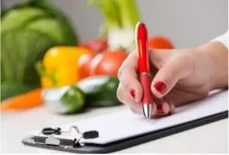 Woman writing on clipboard surrounded by fresh vegetables