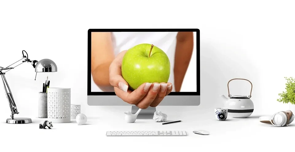 Hand holding a green apple through a computer screen representing virtual nutrition consultations